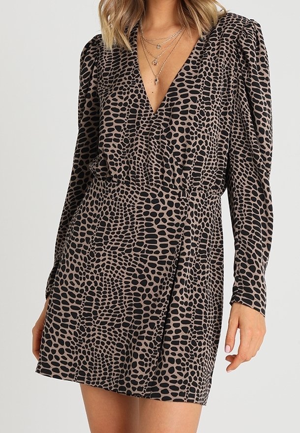 Femme portant une mini-robe à manches longues imprimée animalière marron et noire, avec un décolleté en V profond et des colliers en or superposés.