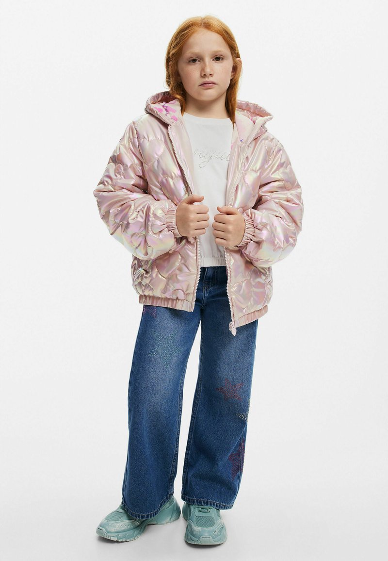 Rosa iridiserande puffjacka med blommönster, försedd med huva och dragkedja fram. Matchad med blå vida jeans och turkosa sneakers.