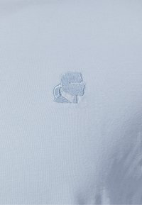 Tissu bleu clair avec un petit profil brodé d'une personne portant des lunettes de soleil et une queue de cheval en fil bleu assorti.