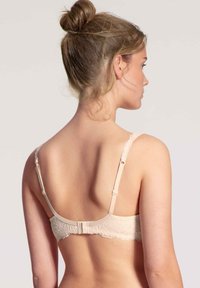 Beige bh met kant op de rug en verstelbare bandjes, voorzien van een haaksluiting en een gladde textuur, met bloemenpatroondetails.