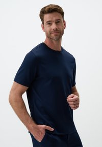 Granatowa koszulka z krótkim rękawem wykonana z miękkiej tkaniny, z klasycznym okrągłym dekoltem i luźnym krojem, z gładkimi szwami i bez widocznych wzorów.