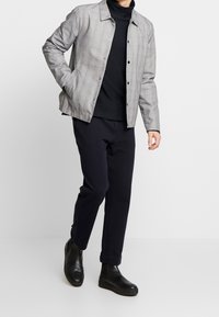Szary w kratę żakiet z kołnierzem, noszony na czarnym golfie, w połączeniu z granatowymi spodniami i czarnymi botkami za kostkę. Gładka faktura materiału.