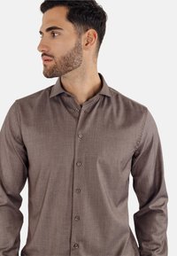 Brun skjorte med lange ermer og knapper, laget av teksturert stoff, med moderne krage, knappelukking og subtilt mønster.