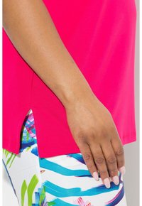 Fuchsia t-shirt met korte mouwen en zij-slits, gecombineerd met meerkleurige shorts met een patroon, voorzien van blauwe strepen en groene bloemaccenten.