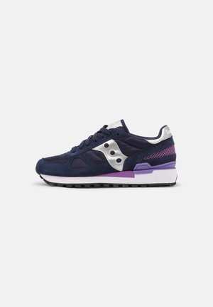 Zapatilla Saucony azul marino y púrpura con parte superior de malla y ante, logo plateado, suela exterior negra y entresuela blanca sobre un fondo claro.
