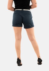 Navyblauwe katoenen shorts met opgerolde zomen, voorzien van een gemusterde tailleband en twee achterzakken. G gedragen met zwarte hoge hakken.