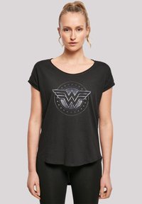 Svart kortermet t-skjorte laget av myk stoff med et sølvfarget Wonder Woman-logo med vinger og sirkelstjerne-design. Rund hals.