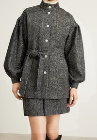 Textured gray and gold woven jacket with oversized sleeves, button closure, and matching skirt. Features a tied belt accent.