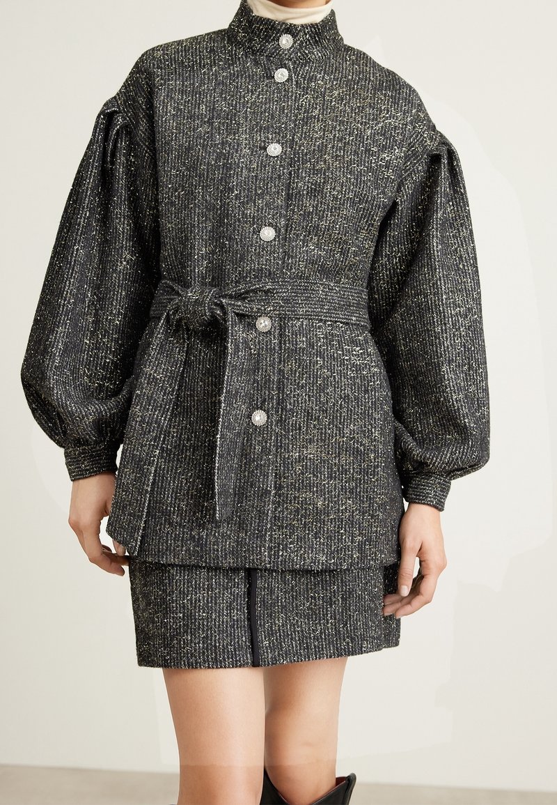 Texturierter grauer und goldener gewebter Blazer mit übergroßen Ärmeln, Knopfverschluss und passendem Rock. Verfügt über einen akzentuierenden gebundenen Gürtel.