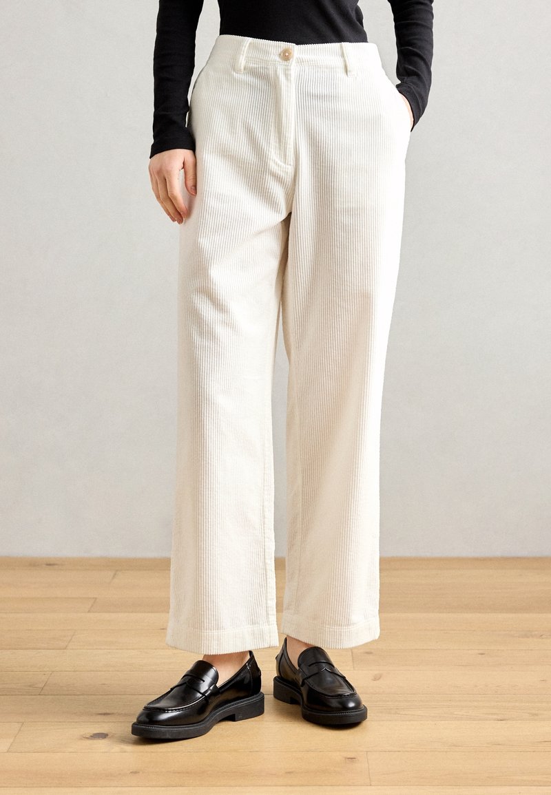 Pantalons larges en velours côtelé crème avec des rayures verticales, dotés d'une fermeture à bouton et de poches latérales, associés à des mocassins en cuir noir.