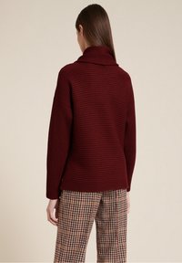 Burgundy-randig tröja med vikt krage, breda ärmar och avslappnad passform, ihop med byxor i brunt och vitt houndstooth-mönster.