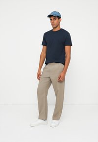 Maglietta blu navy a maniche corte, pantaloni beige a vestibilità rilassata e sneakers bianche. Un cappellino azzurro chiaro completerà l'outfit casual.