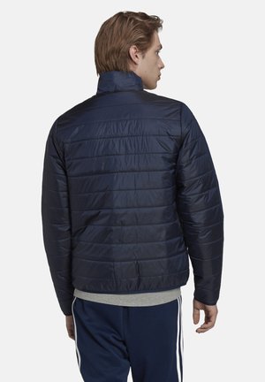 Marineblauwe gewatteerde jas met een hoge kraag, gequiltde textuur en elastische onderrand. Beschikt over een gladde, glanzende afwerking en minimale hardware.