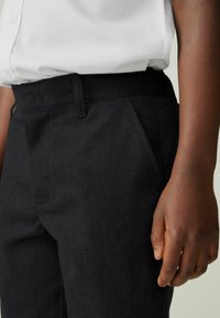 Schwarze Baumwollhose mit glatter Textur, gerader Schnitt, flache Vorderseite und Seitentaschen, kombiniert mit einem weißen Hemd mit Kragen.