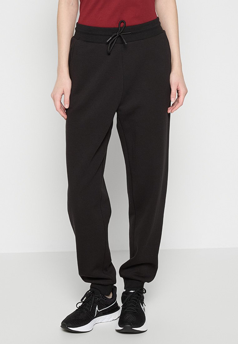 Pantalons de survêtement noirs en tissu doux, dotés d'une taille élastique avec cordon de serrage, de poches latérales et d'une coupe décontractée. Adaptés pour un usage décontracté.