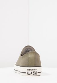 Baskets en toile vert olive avec une finition texturée, semelle en caoutchouc blanche et accents noirs. Présente le logo "Converse All Star" sur le talon.