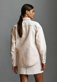 Valkoinen vaaleanpunainen löysä denimpaita, jossa on nappihihansuut ja kaareva helma, yhdistettynä vastaavaan mini-hameeseen, jossa on rispaantuneet reunat.