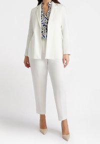 Bílý elegantní blejzr přes modro-bílou vzorovanou blůzu, doplněný bílými slim-fit kalhotami a nahými špičatými lodičkami. Hladký povrch tkaniny.