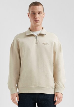 Lichtbeige zip-hals sweatshirt met lange mouwen, ribgebreide manchetten en een rechte onderkant. Voorzien van geborduurde tekst op de linkerkant van de borst.