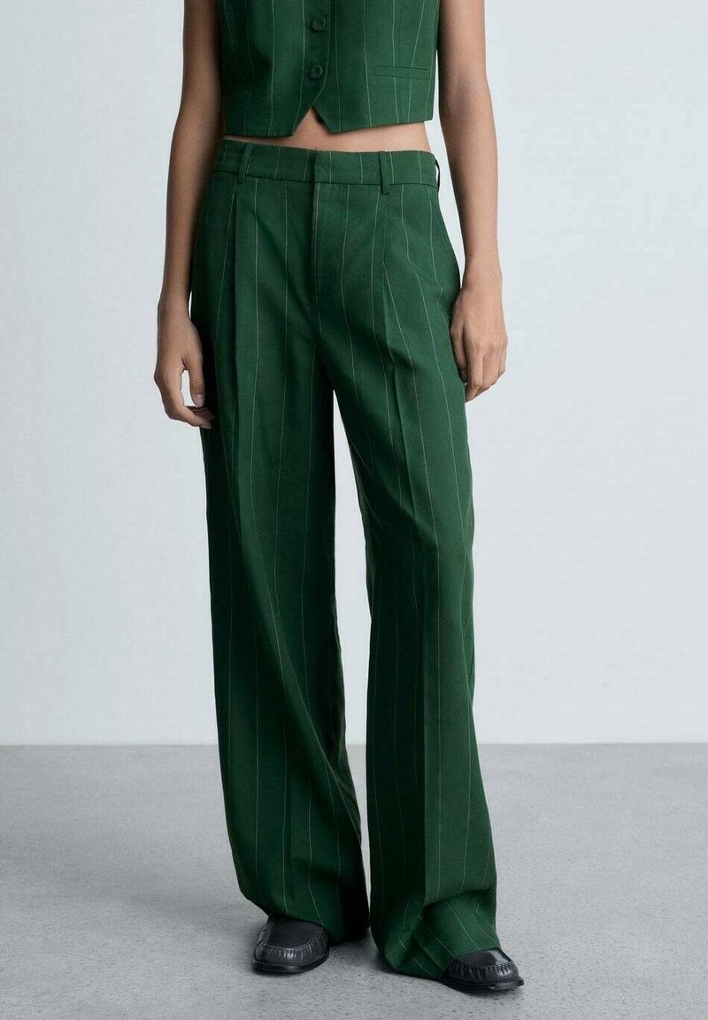 Pantalon large à rayures vertes en tissu lisse, doté d'une taille haute et de plis à l'avant, associé à des chaussures noires texturées.