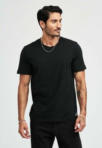 Svart kortärmad t-shirt i texturerad bomull, med rundad halsringning och en liten logodetalj i nederkant. Bärs med mörka jeans.