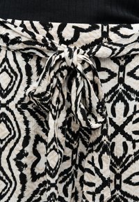 Ceinture en tissu nouée avec motif géométrique noir et beige sur un vêtement assorti à motif et un top noir.
