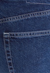 Tmavě modrý denimový materiál s hladkou texturou, vybavený zadní kapsou a bílým prošitím podél švů.