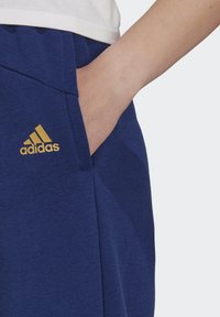 Donkerblauwe sportbroeken van zachte stof, met een zijzak en een gouden adidas-logo op het linker heupgebied.