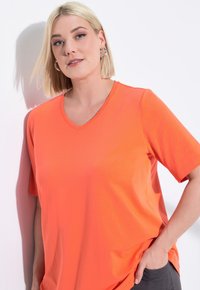 Camiseta de algodón de color naranja brillante, de cuello en V, manga corta y corte holgado. Textura suave con costuras mínimas y un diseño relajado y casual.