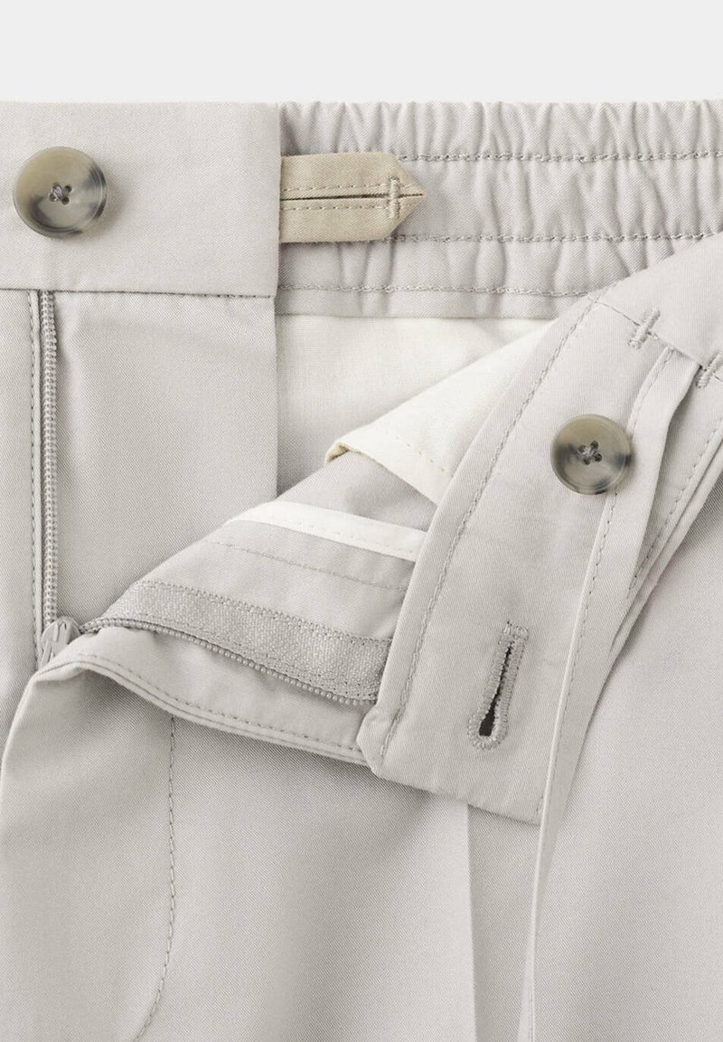 Close-up of beige pants waistband showing button, buttonhole, zipper, adjustable elastic band, and interior stitching details.