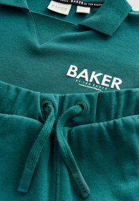 Tyrkysová bavlnená polokošeľa s V-výstrihom a bielym logom "BAKER", v kombinácii s ladiacimi teplákmi s elastickým pásom a šnúrkou.