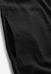 Tissu noir avec une finition texturée, présentant des coutures contrastantes le long des bords. Le matériau semble léger et doux.
