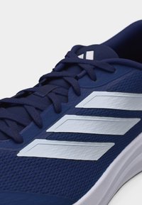 Chaussure de sport bleu marine avec un design à trois bandes blanches, des lacets noirs et une tige en maille texturée, vue de côté et du dessus.