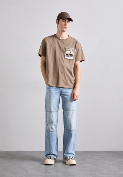 Pruun puuvillane T-särk, millel on rinnakott; helesinised lapiga teksad; beežid kingad mustade paeltega; pruun müts. Pehme tekstuur, mugav lõige.