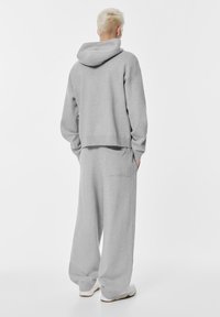Sivý, prehnaný mikina s kapucňou a vreckom na chrbte; spárovaná s rovnako sivými, širokými teplákmi; oboje vyrobené z mäkkej, textúrovanej látky.