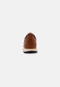 Sneaker en cuir marron avec une finition texturée, dotée d'un col rembourré et d'une semelle beige contrastante. Semelle extérieure en caoutchouc noir visible.
