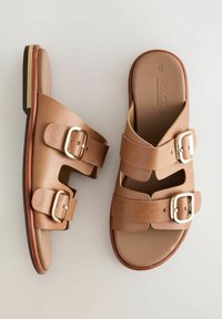 Brune lædersandaler med glidende design, dobbelt spænde-stropper, åbne sider og en brun sål. Glat tekstur med minimal syning.