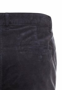 Donkerblauwe corduroy broek met een achterzak met klep, gestructureerd oppervlak en een standaard tailleband. Subtiele glans zichtbaar op de stof.