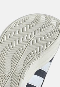 Gumeni đonovi s zigzag uzorkom. Bijela boja s teksturiranim područjima i sivim naglascima. Ima bočne pruge kontrastne boje.