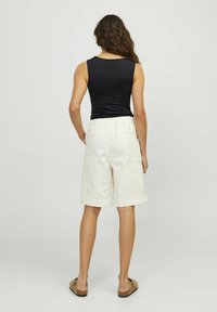 Top nero senza maniche, pantaloni corti crema con vita elastica, tessuto liscio, lunghezza al ginocchio. Sandali color cammello. Tasche visibili sui pantaloni corti.