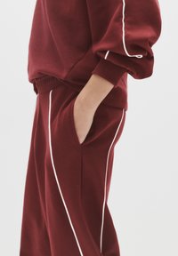 Bordeaux sweatshirt og bukser sæt med hvid piping detaljer. Blødt stykke stof, løs pasform og sidelommer på bukserne. Elastiske manchetter og talje.