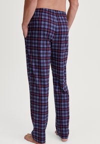 Geruite pyjamabroek in blauw, zwart en rood met een elastische tailleband, twee zijzakken en een losse pasvorm, zichtbaar vanaf de achterkant.