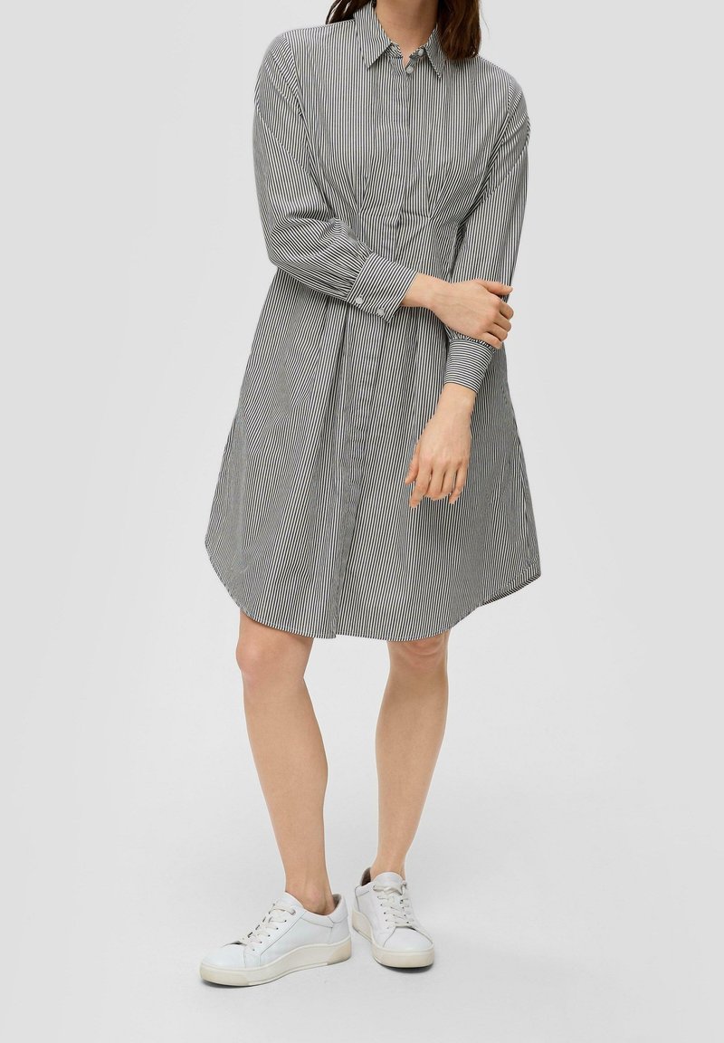 Robe-chemise rayée avec col, manches longues, boutonnée sur le devant et coupe ample, associée à des baskets blanches. Le motif présente des rayures verticales étroites.