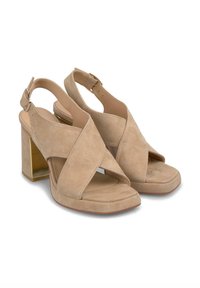 Sandales à talons en suède beige avec un bout ouvert, un design à brides croisées, une boucle à la cheville et un talon en bloc à teinte dorée. Texture lisse et style minimaliste.