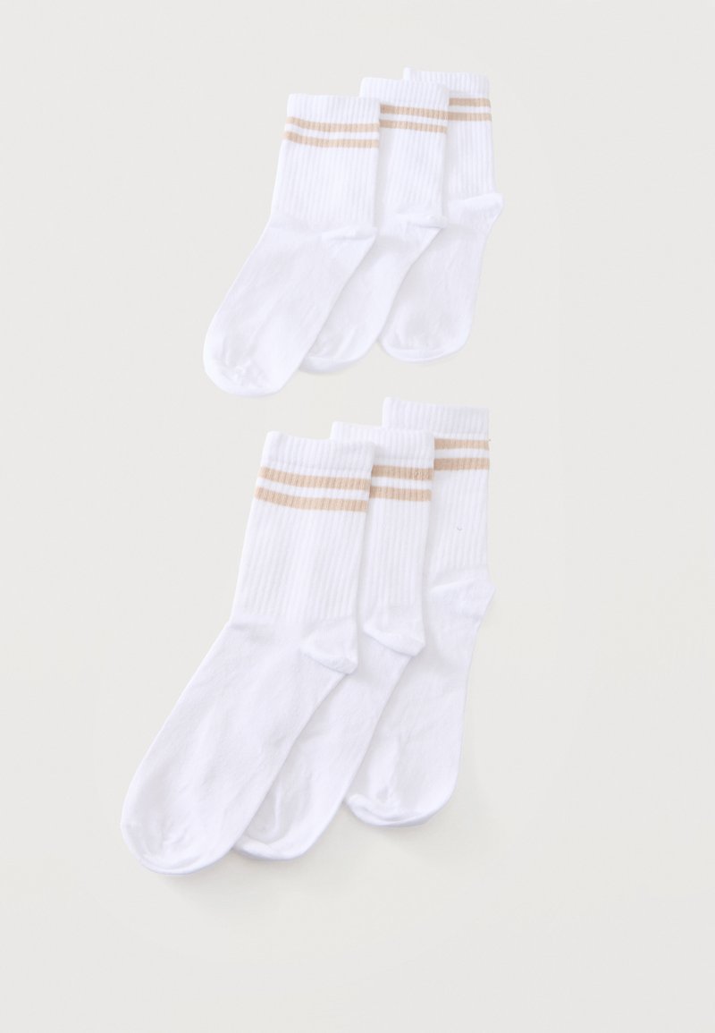 Sept chaussettes blanches montantes avec deux bandes beiges près du haut, disposées en deux groupes qui se chevauchent sur un fond uni.