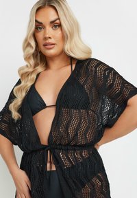 Svart öppen stickad överdel med en vågig design, avslappnad passform och korta ärmar, samlad vid midjan med en dragsko.