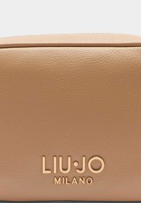 Kerge pruun nahast kott, millel on tekstuurne pind, esiküljel on selgelt nähtav kuldne kiri "LIU·JO MILANO".