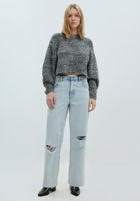 Grauer, gestrickter, verkürzter Pullover mit strukturiertem Finish, kombiniert mit hellblauen, hochtaillierten Jeans mit zerrissenen Knien und schwarzen Stiefeletten.