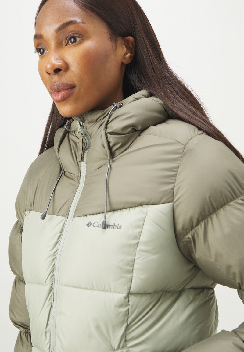 Olivgrüne Pufferjacke mit einem hellgrünen Einsatz, ausgestattet mit einem Reißverschluss, einer Kordelzugkapuze und dem Columbia-Logo auf der Brust.