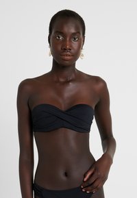 Črn bandeau bikini zgornji del s zasukanim sprednjim delom. Gladek material, minimalističen slog, elastična prileganja, v kombinaciji s usklajenim spodnjim delom.